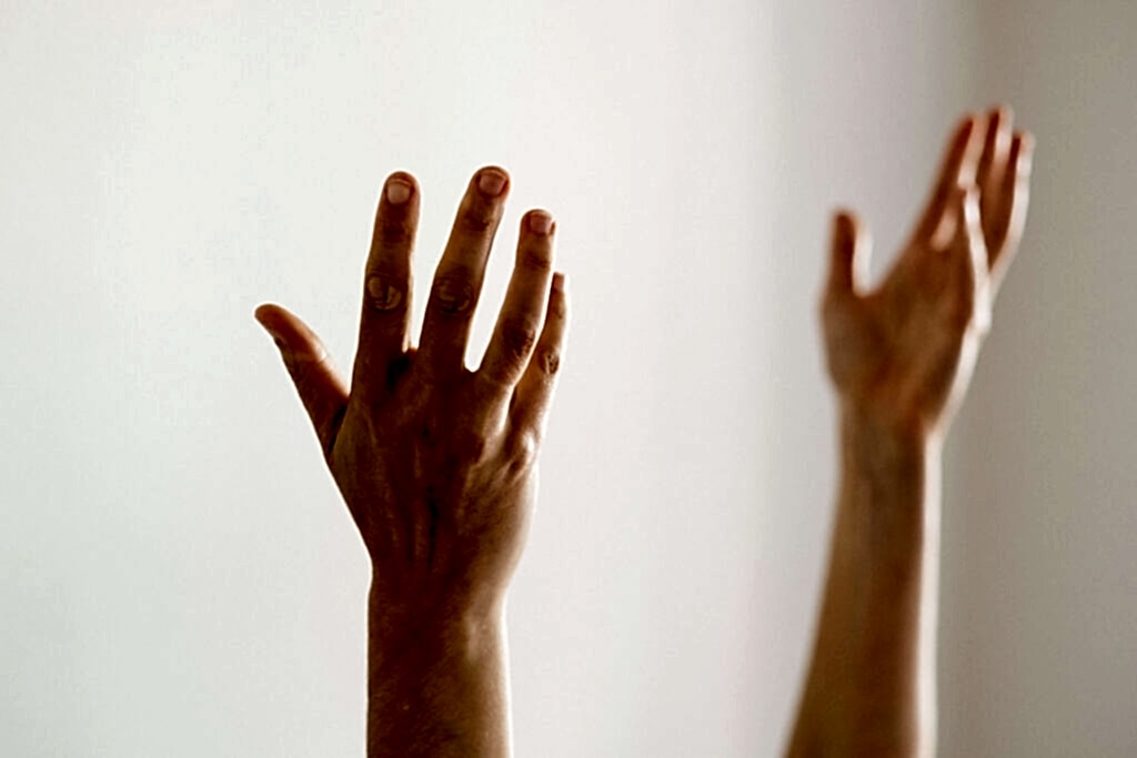 Two hands reach up against a white wall