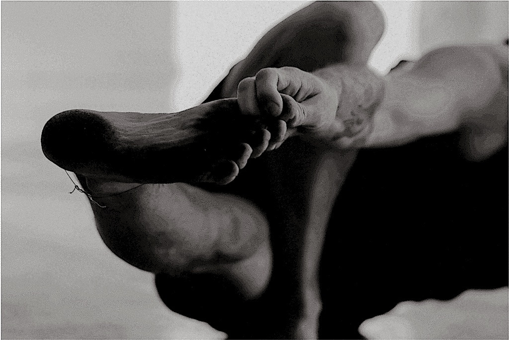 A black and white photo of the underside of a foot. The person is holding their big toe with their pointer fingers.
