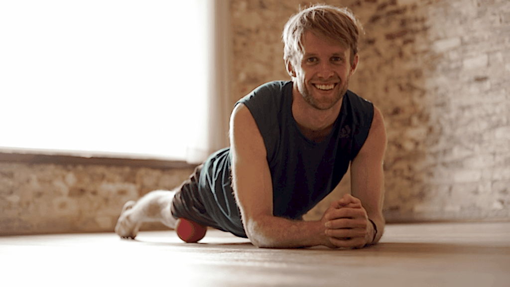 A man with blond hair rolls his hip flexor out using a trigger ball.
