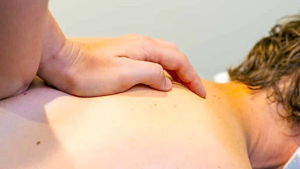 a hand massages a persons back in a physio session