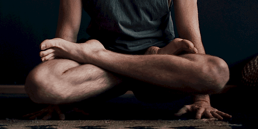 A man holds himself up on his hands while his legs hover crossed