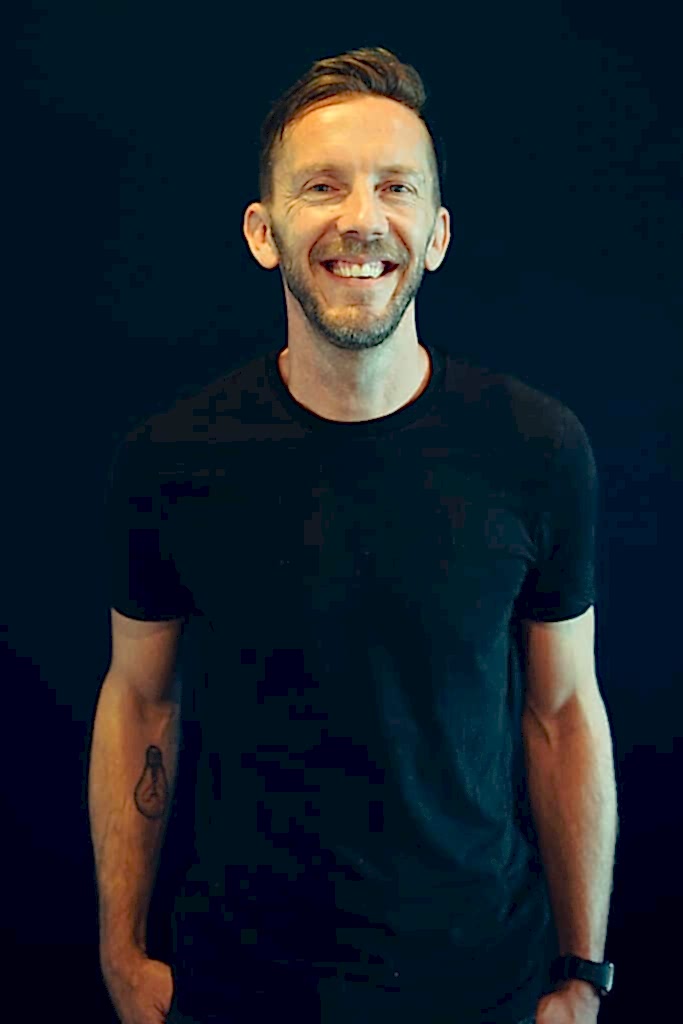 a man in a black t shirt smiles at the camera