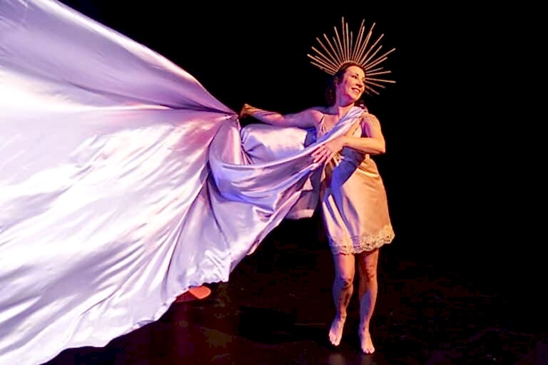 A woman stands on stage holding a large piece of purple fabric